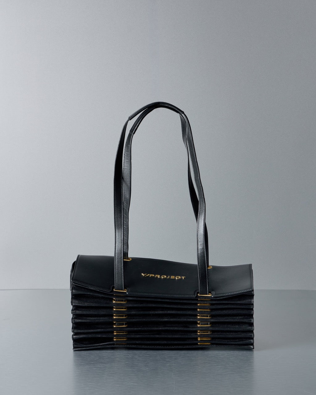 Black Y/Project handbag with gold accents on a gray background