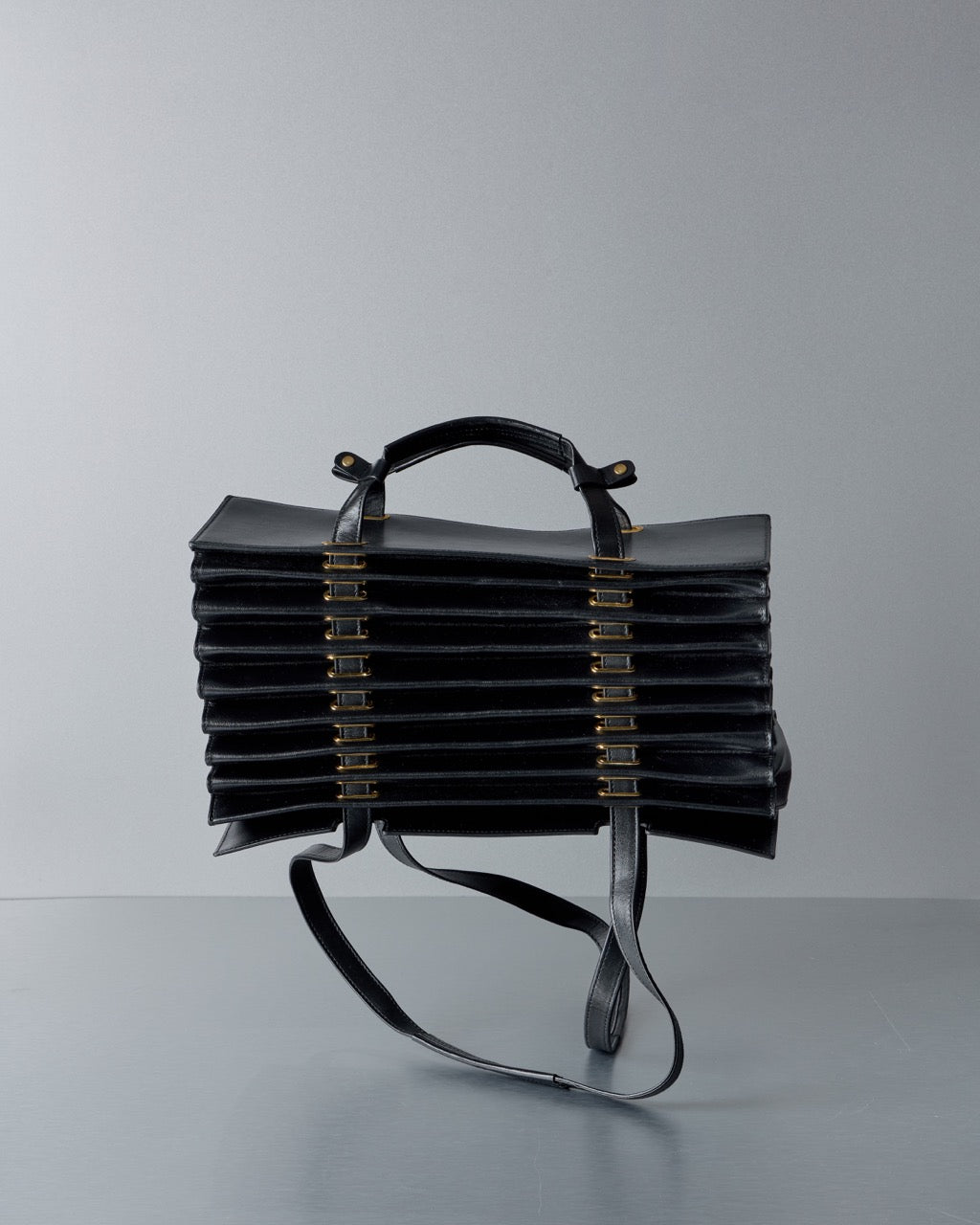 Black leather Y/Project handbag with a unique design on a gray background