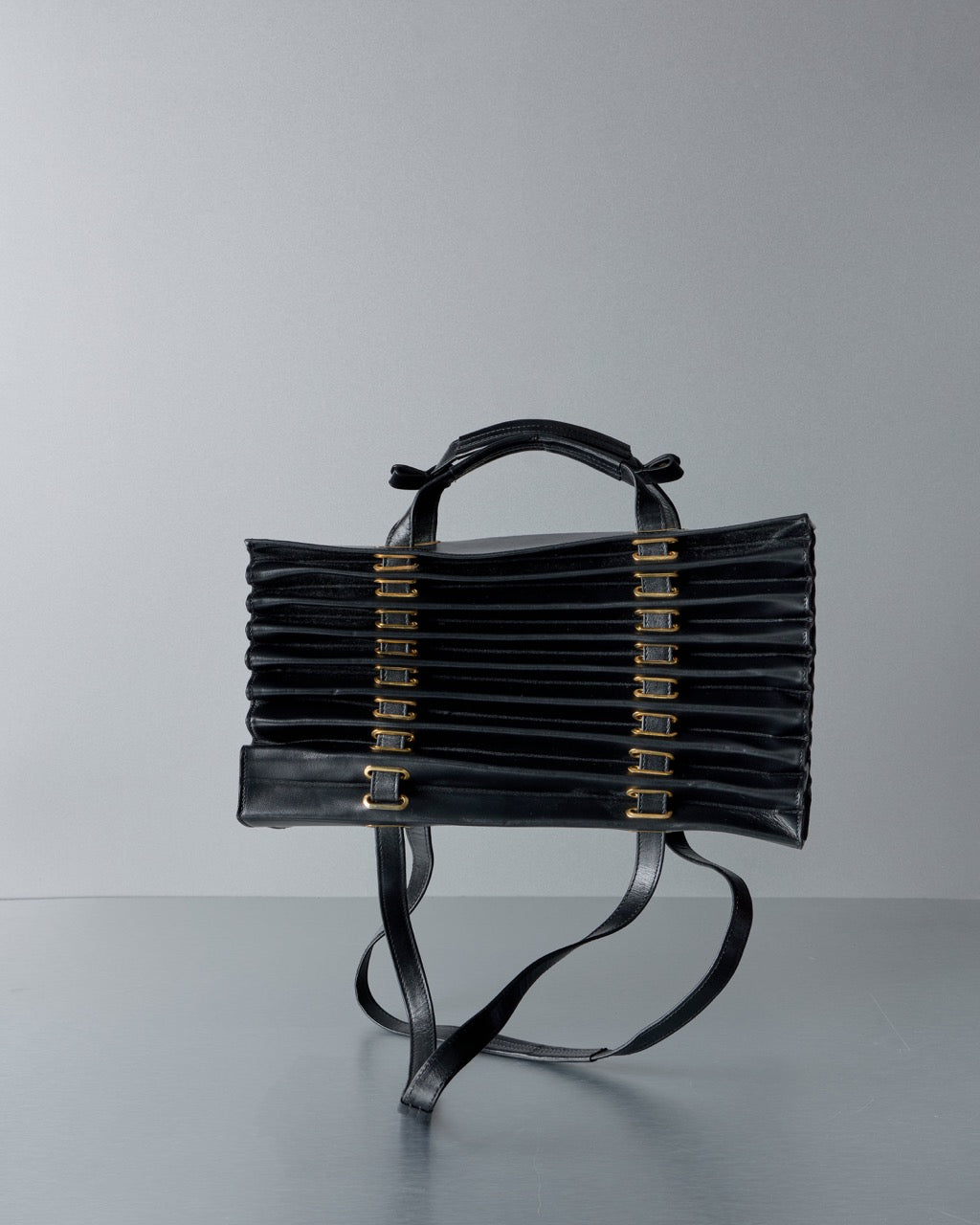 Black Y/Project handbag with gold accents on a gray background