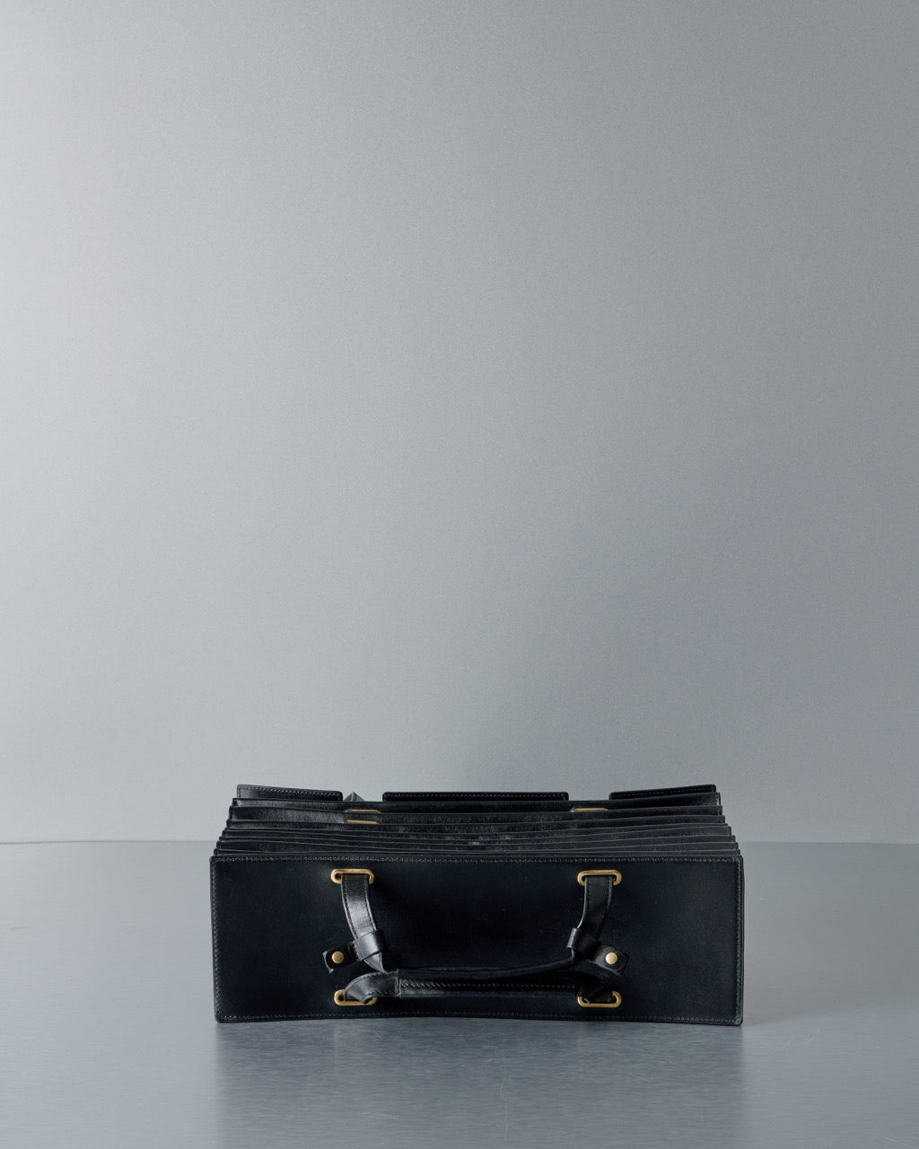 Black leather Y/Project bag with gold hardware on a gray surface and background
