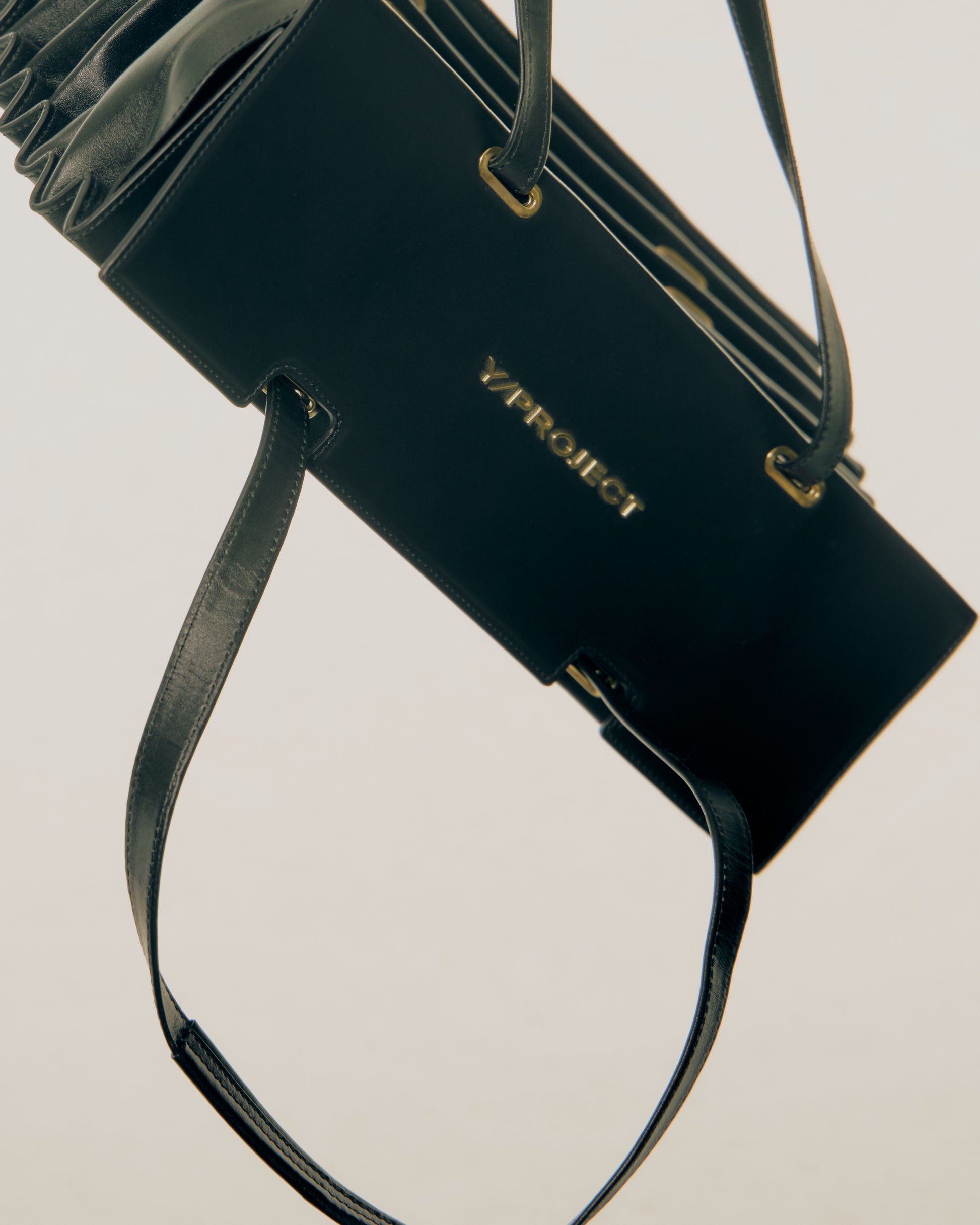 Black Y/Project handbag with gold accents on a light gray background