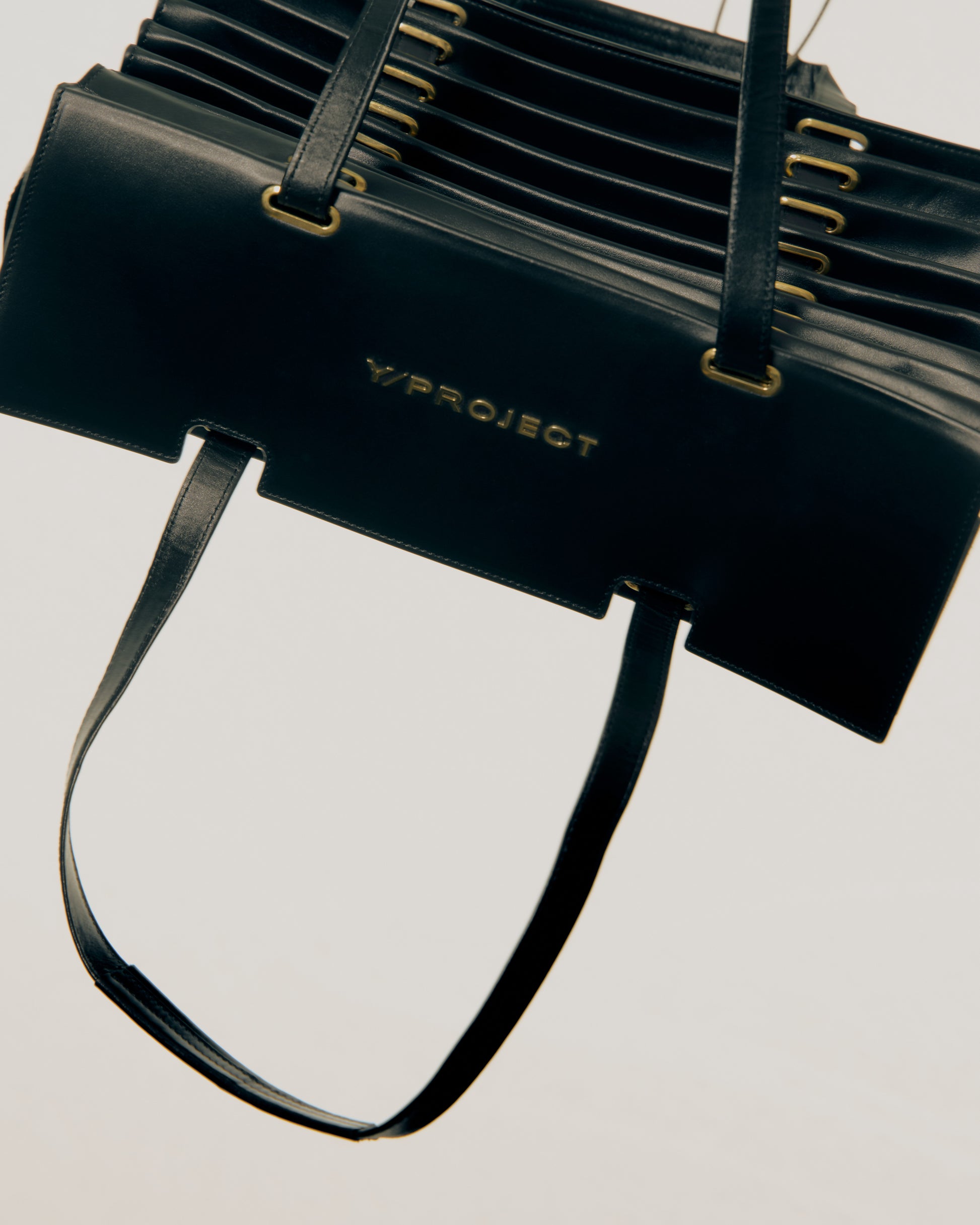 Black Y/Project handbag with gold accents on a light gray background