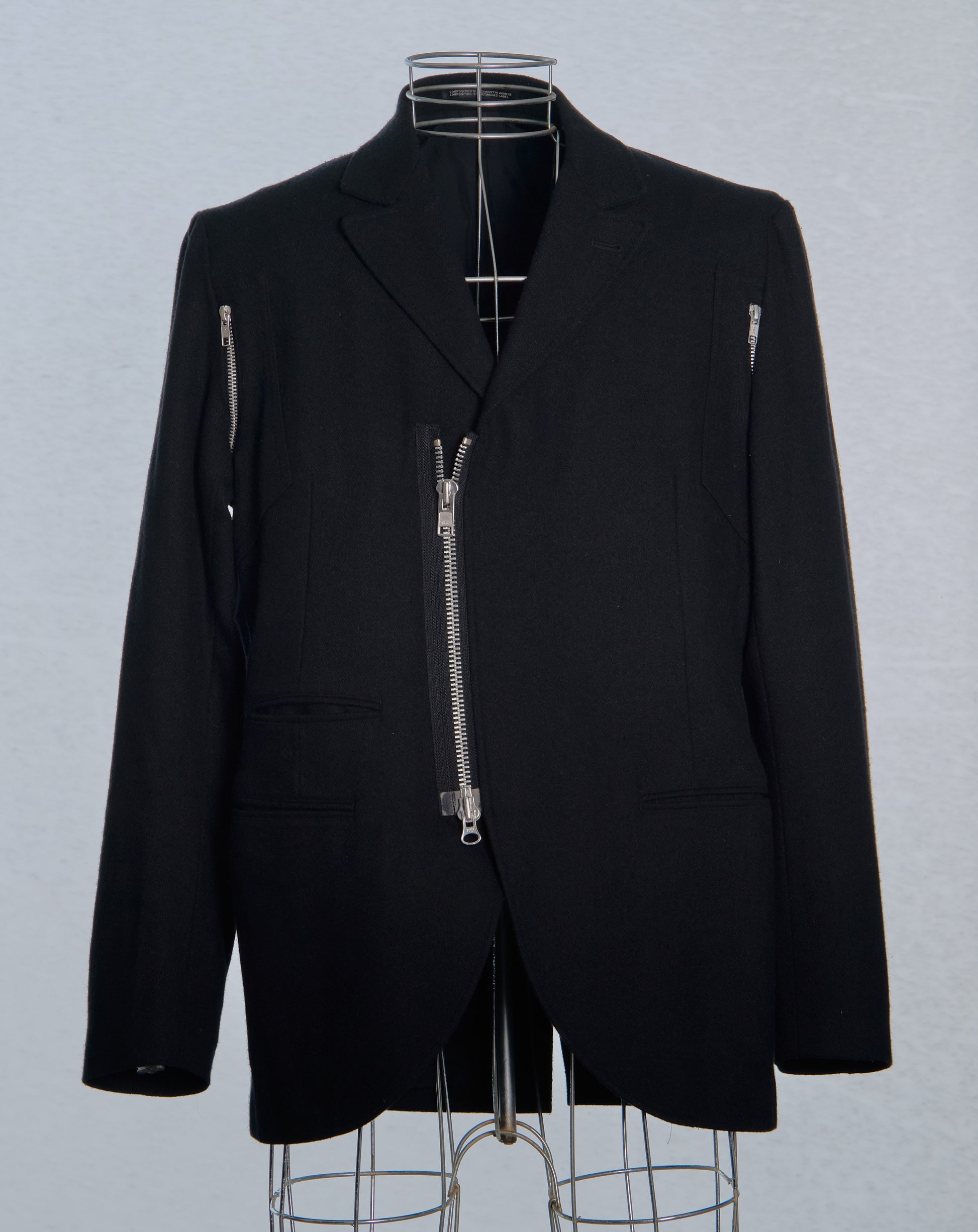 Black Yohji Yamamoto jacket with zippers on a mannequin against a gray background