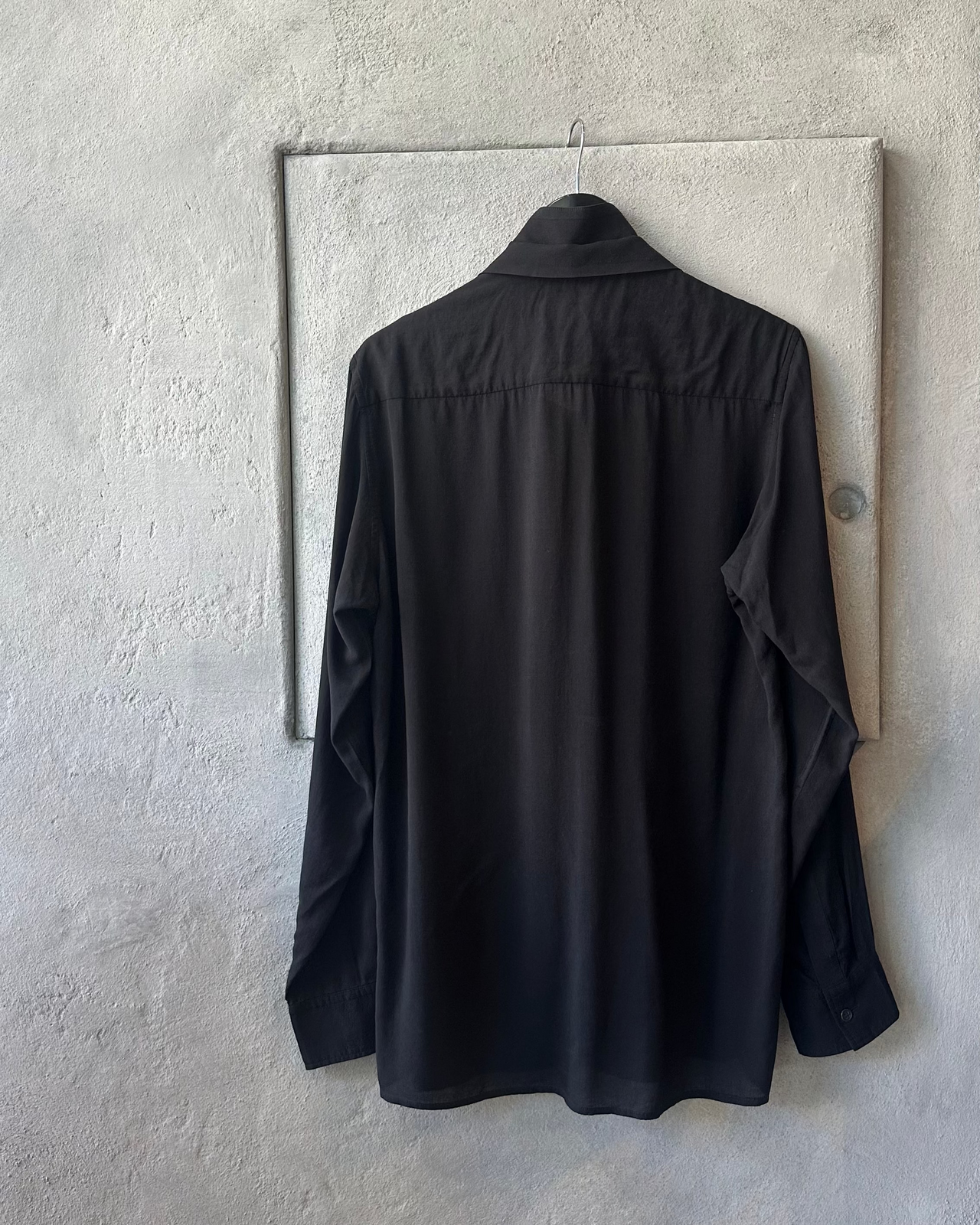 Black Yohji Yamamoto shirt hanging on a hook against a textured wall