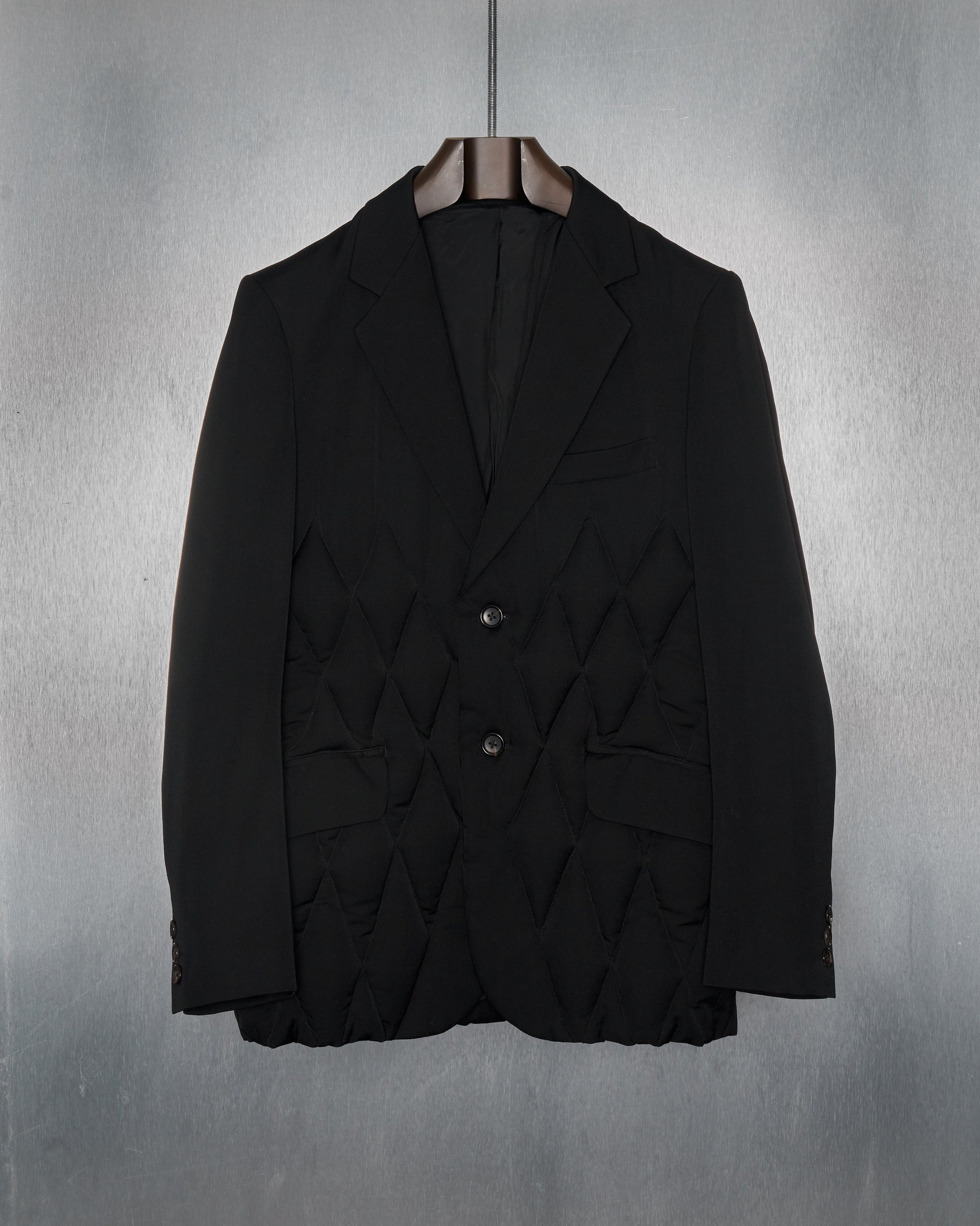 A heavyweight quilted Yohji Yamamoto blazer with diamond-quilted cushioning, notch lapel, and two-button front in a dark color, displayed against a textured background.