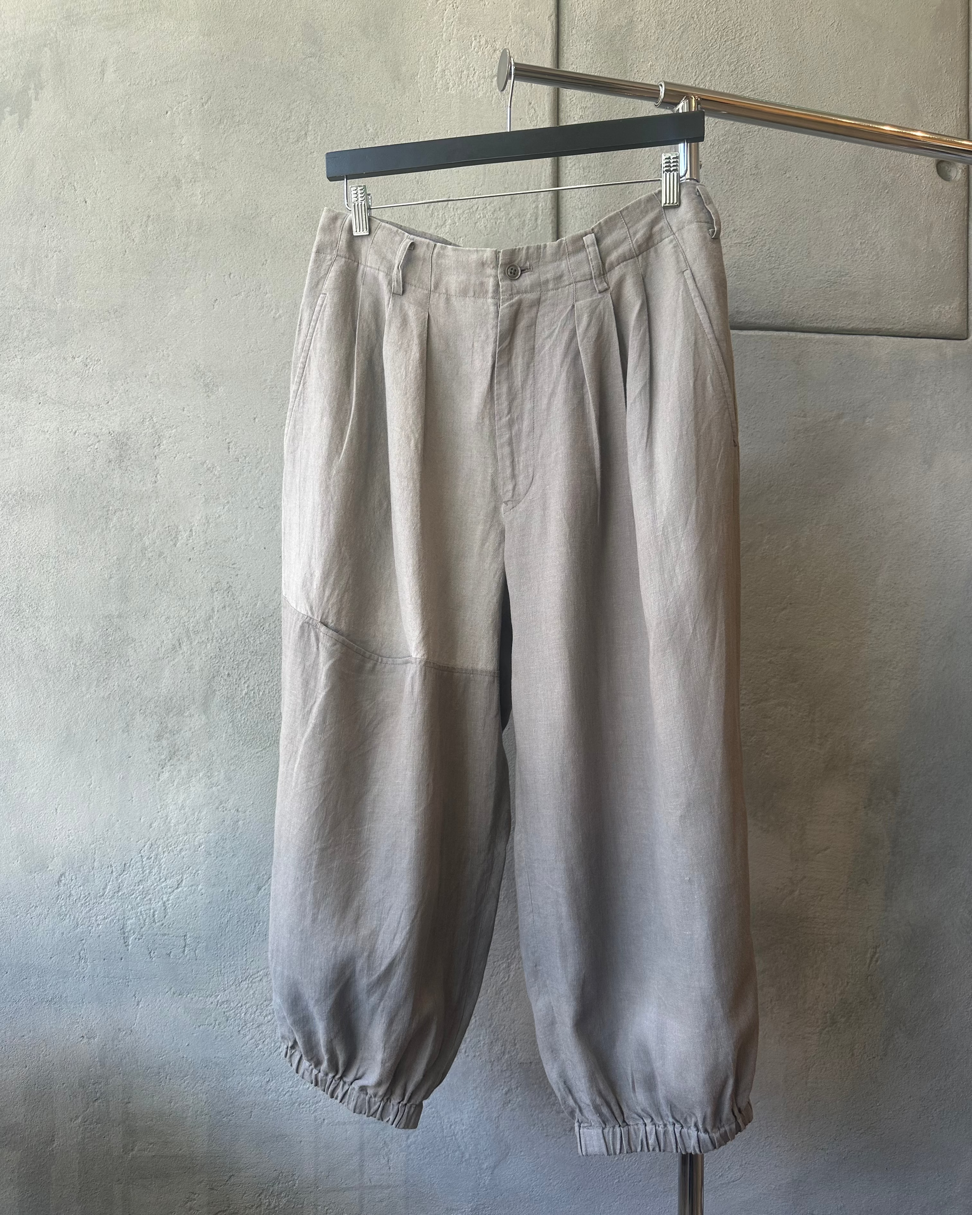 Beige Yohji Yamamoto pants hanging on a rack against a plain wall