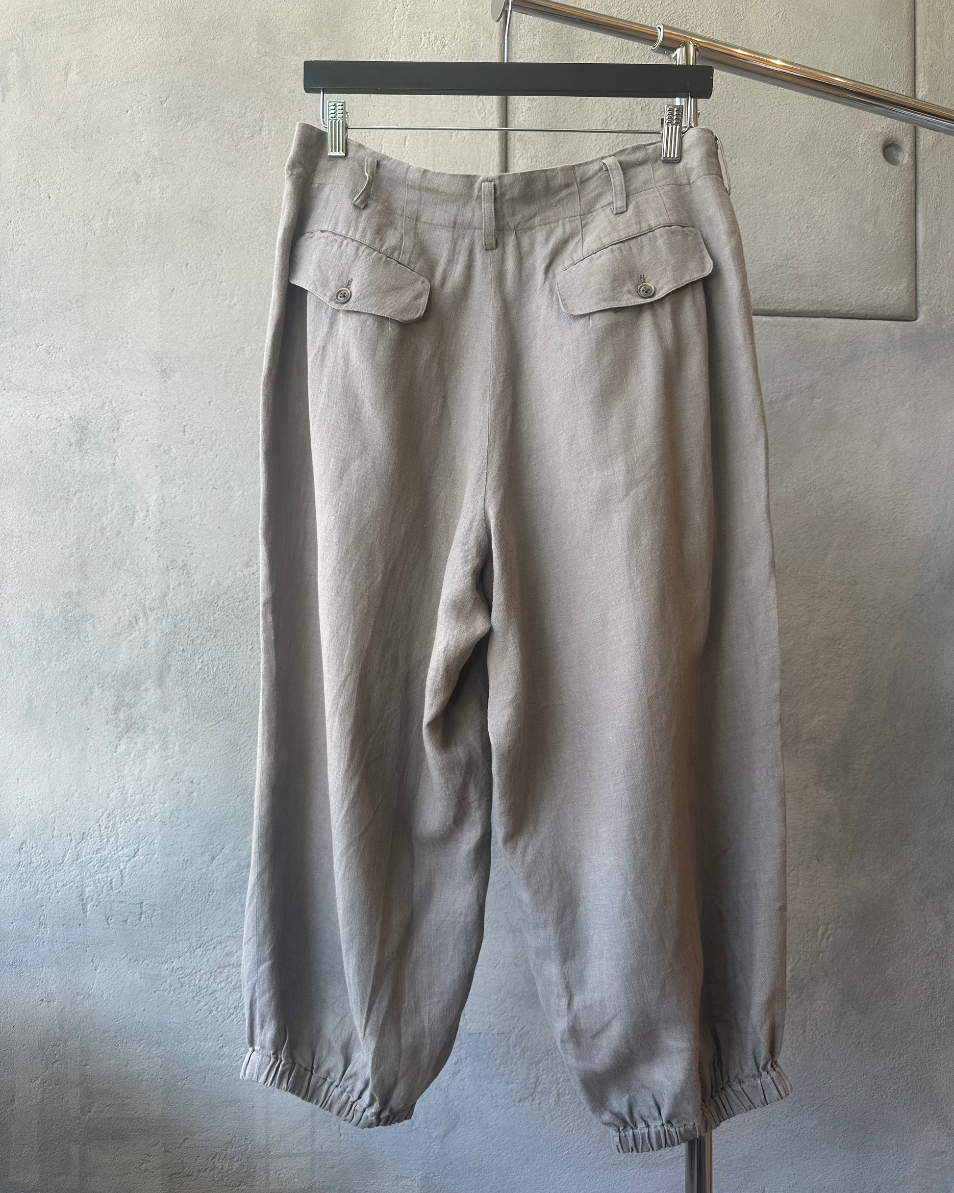 Beige Yohji Yamamoto pants hanging on a rack against a plain background