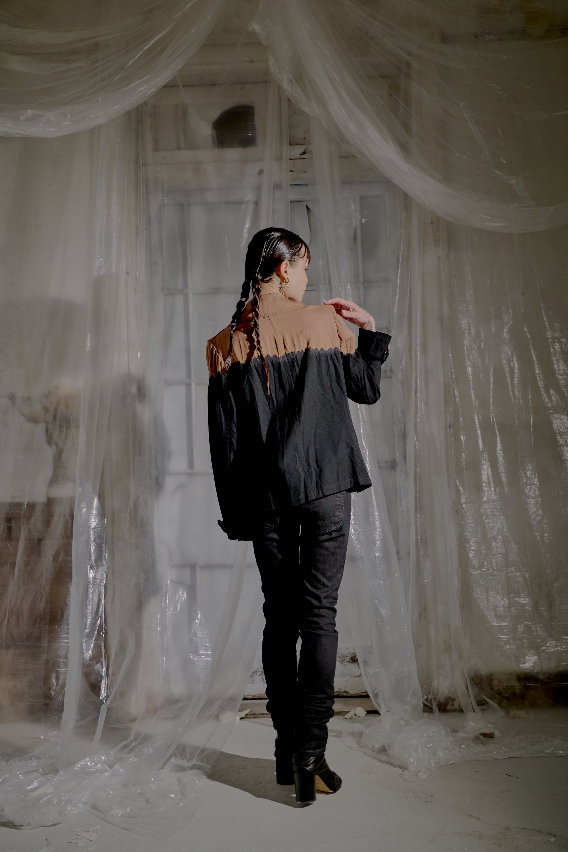 Person wearing a black and brown Y's by Yohji Yamamoto outfit standing in a room with white curtains.