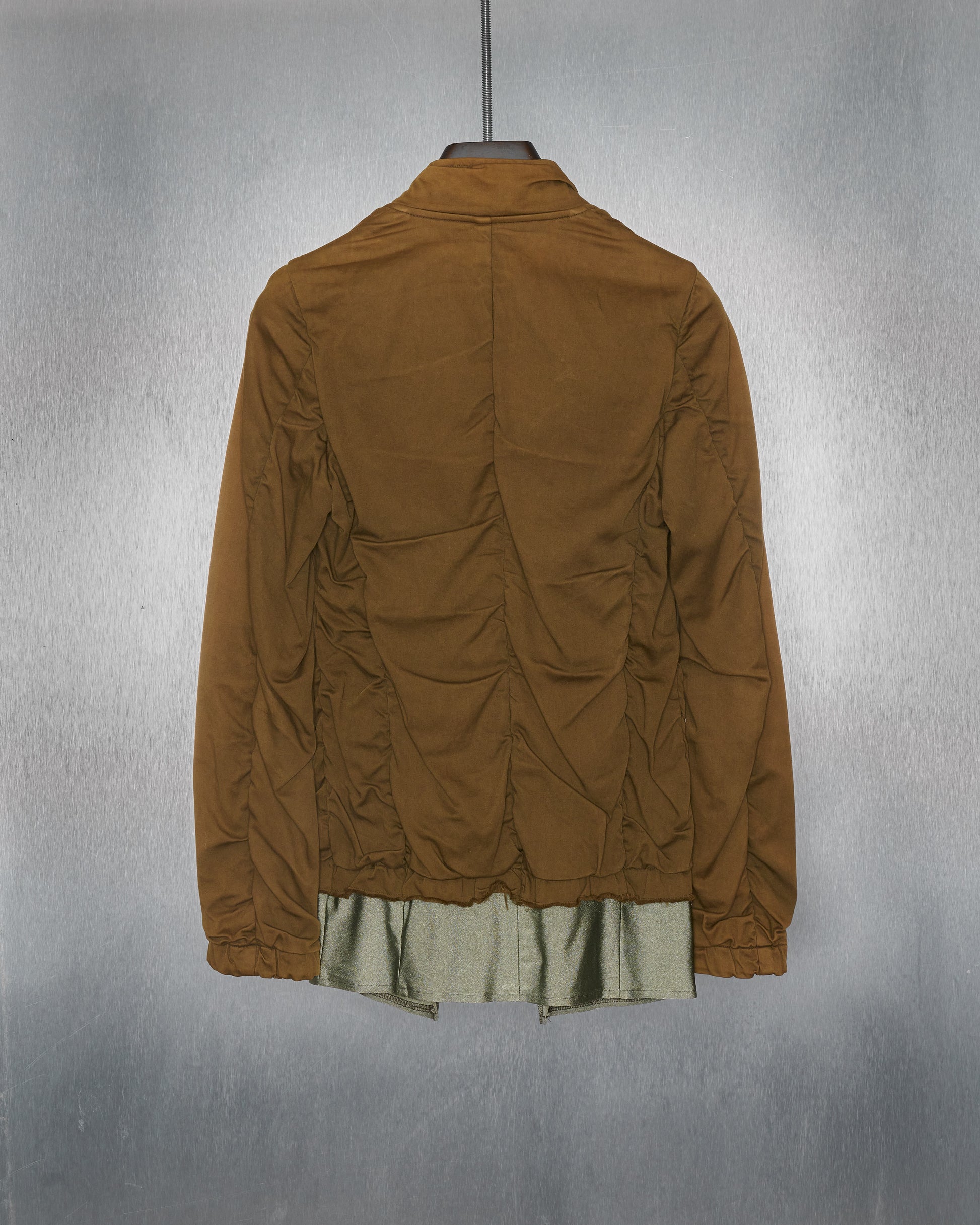 Back of a khaki stretch cotton Comme Des Garcons utility jacket with a glistening internal layer, displayed on a hanger.