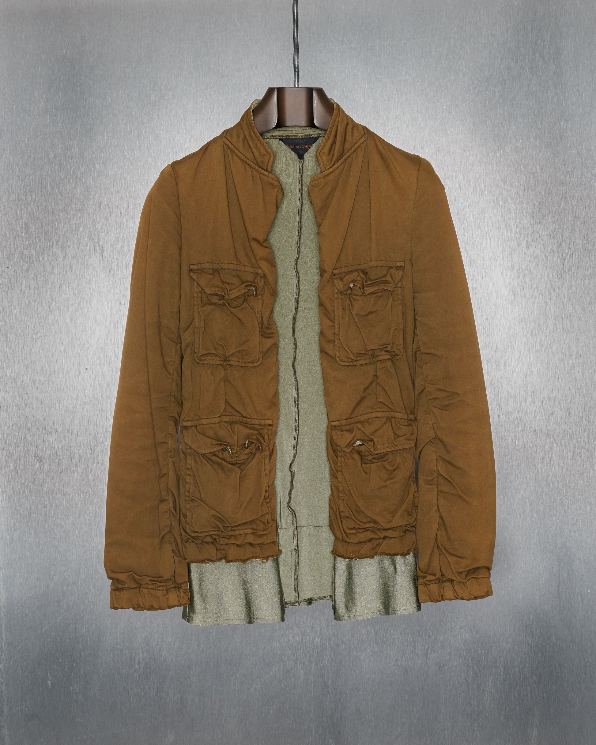A khaki stretch cotton Comme Des Garcons utility jacket with a glistening internal layer, displayed on a hanger.