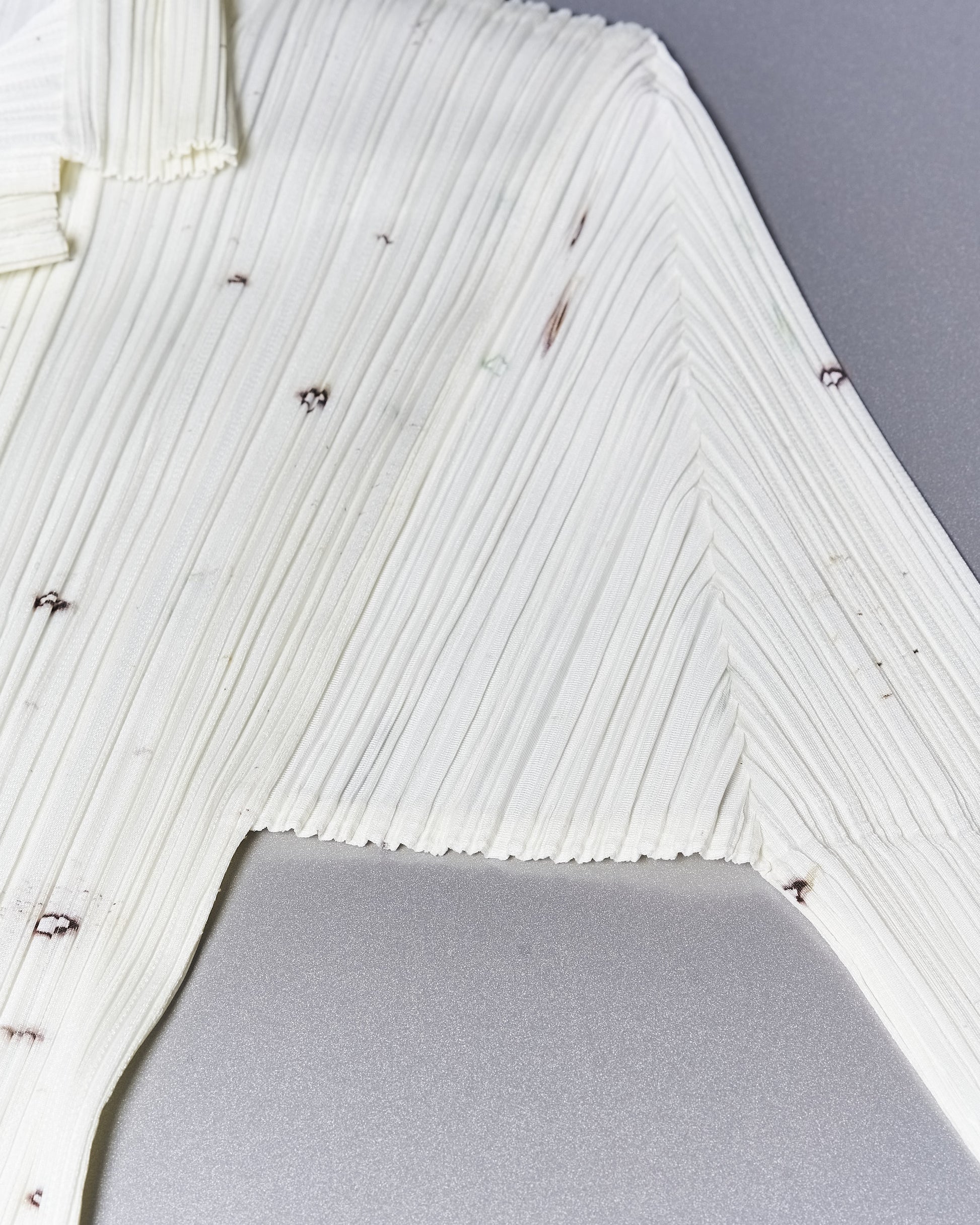 Close-up of a white, pleated fabric with small dark specks on an Issey Miyake dress.