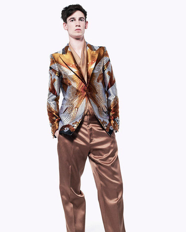 Man wearing a patterned Alexander McQueen jacket and brown pants on a white background