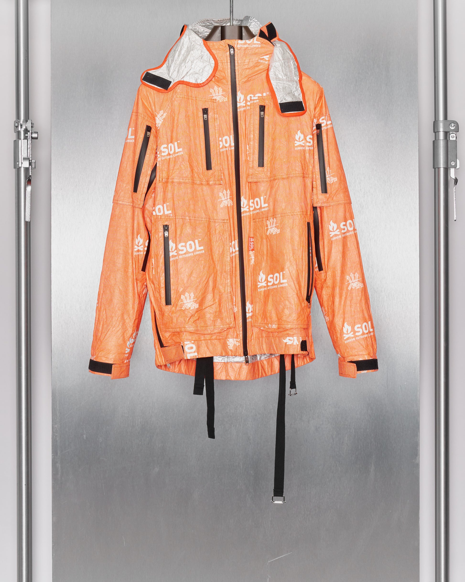 Bright orange jacket by TAKAHIROMIYASHITA TheSoloist  with multiple black zippers and "SOL" logos, hanging against a metallic background. The jacket exudes a sporty, modern vibe.